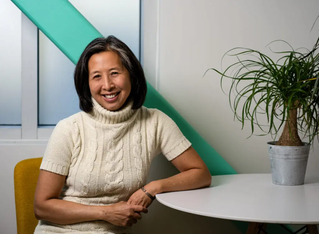 Dr. Michelle Lem smiling in a bright modern workspace with teal accents and natural light.