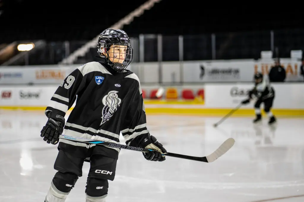 Young hockey player wearing black jersey number 9 practicing on ice rink under bright arena lights.