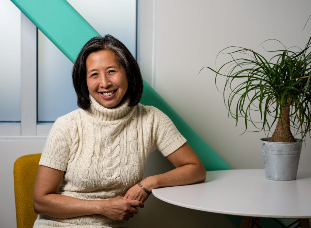 Dr. Michelle Lem smiling in a bright modern workspace with teal accents and natural light.