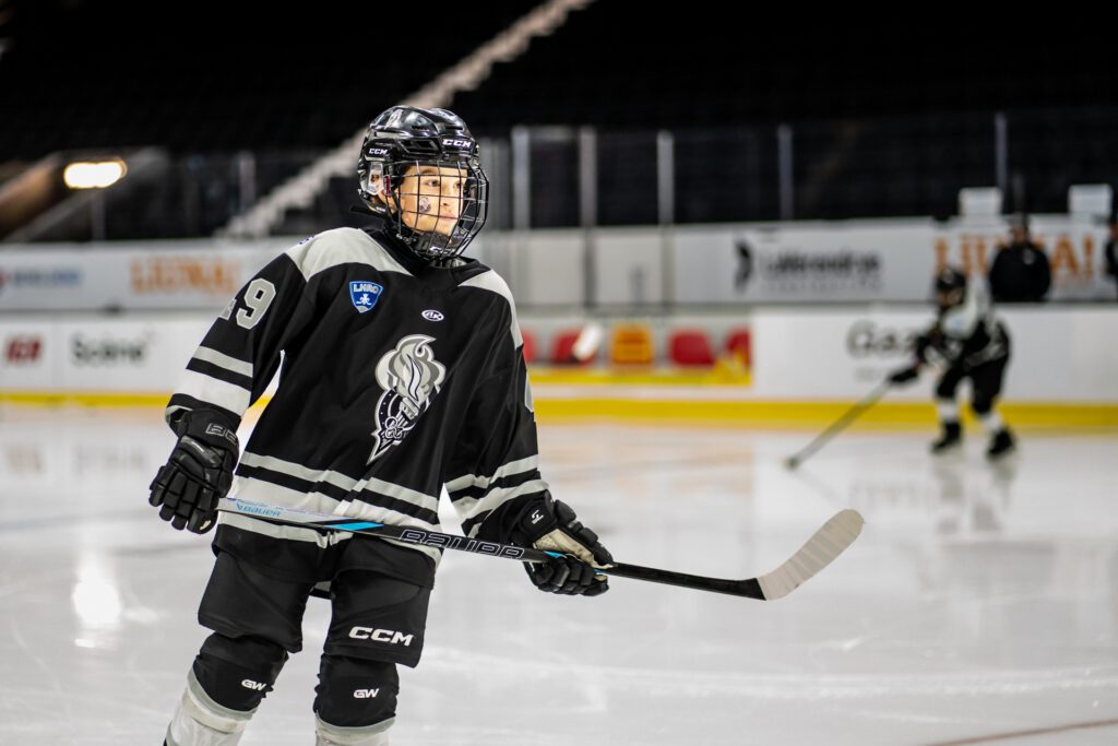 Young hockey player wearing black jersey number 9 practicing on ice rink under bright arena lights.