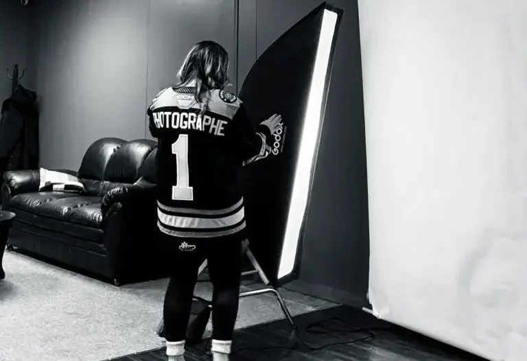 Photographer in black and white jersey adjusts softbox lighting in modern photo studio.