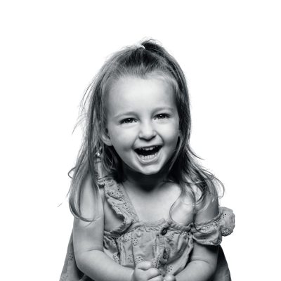 Smiling young girl laughing in black and white portrait, capturing pure childhood happiness.