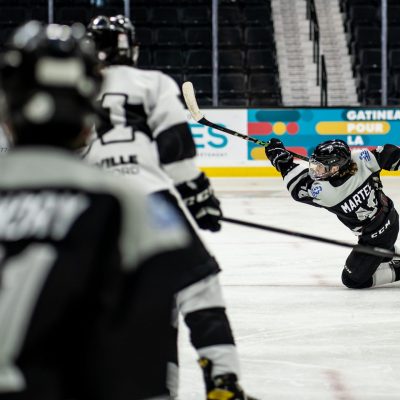 Hockey players in black and white uniforms compete intensely on a brightly lit ice rink.