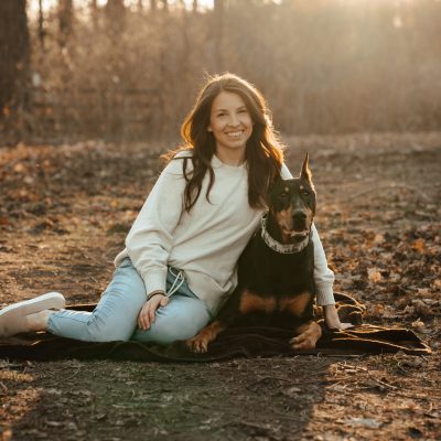 Woman sitting on blanket with loyal dog under golden sunset in peaceful autumn setting.