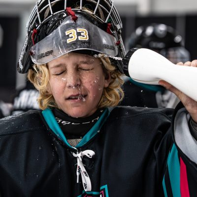 Young hockey goalie #33 rehydrating on the ice rink during an intense game moment.